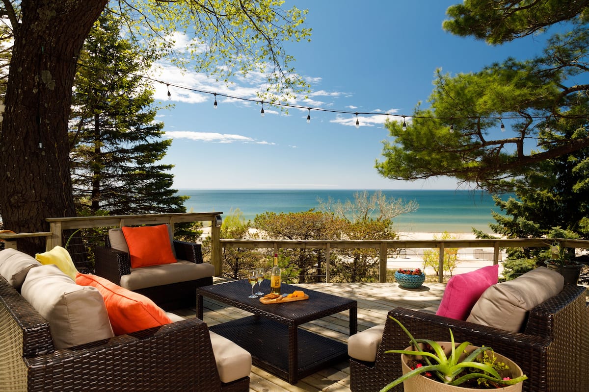 An outdoor seating area with wicker furniture, a table with a bottle and glasses, and a view of the ocean.