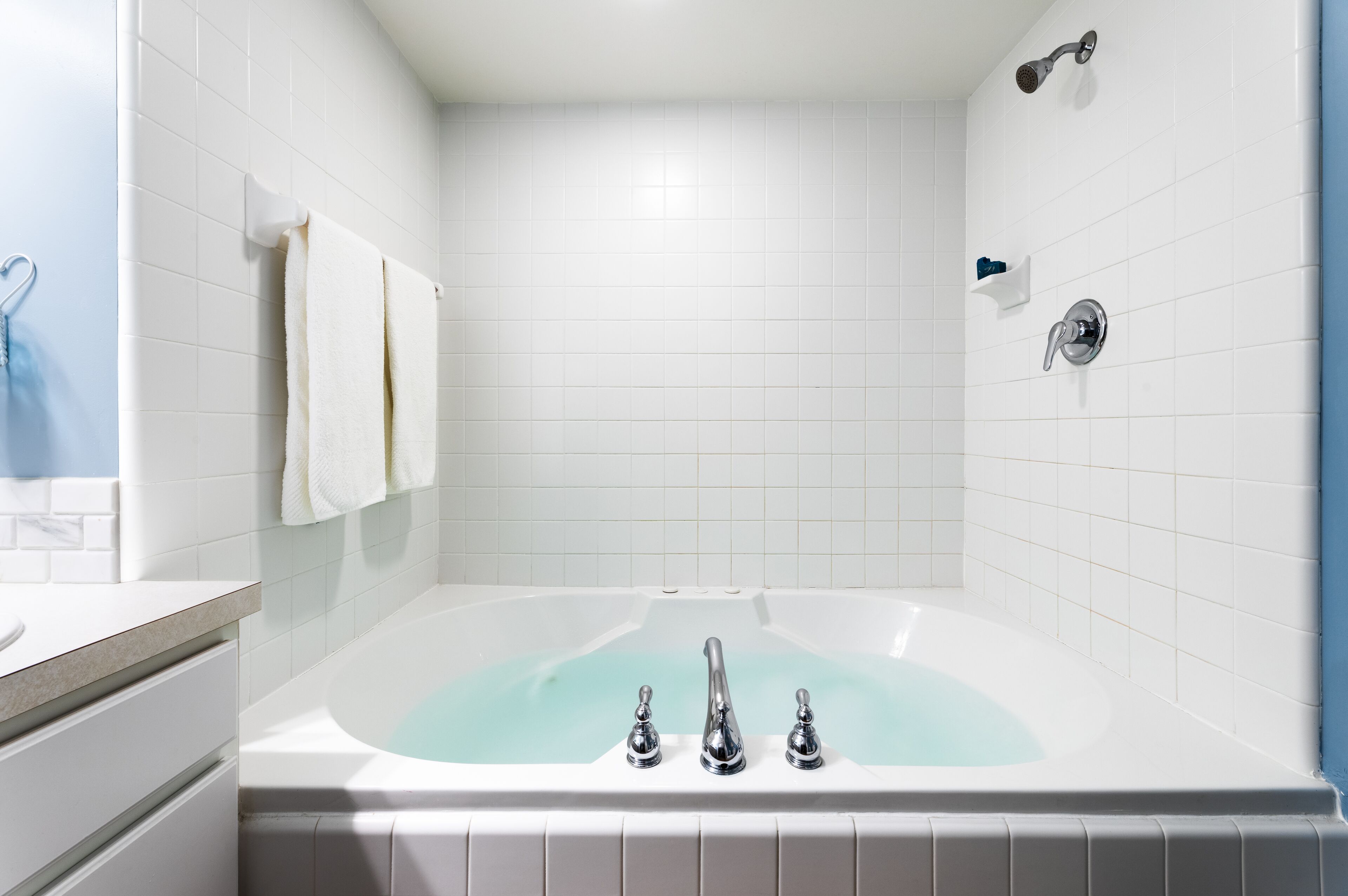 Een moderne badkamer met een vrijstaand bad, witte tegels en een blauwe accentmuur.