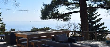 A wooden deck with outdoor furniture, including a table and chairs, overlooking a body of water.