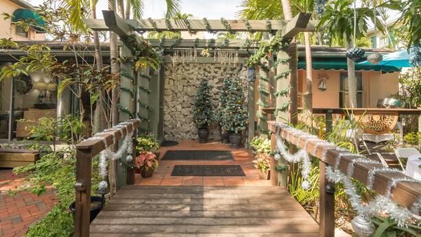 Un sendero de madera que lleva a un muro de piedra con dos árboles de Navidad decorados.