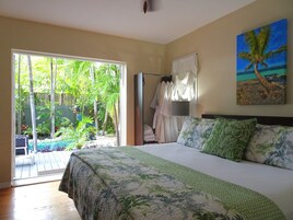 Un dormitorio con una cama grande, vista a un jardín tropical a través de una puerta corredera, y un cuadro de una palmera en la pared.