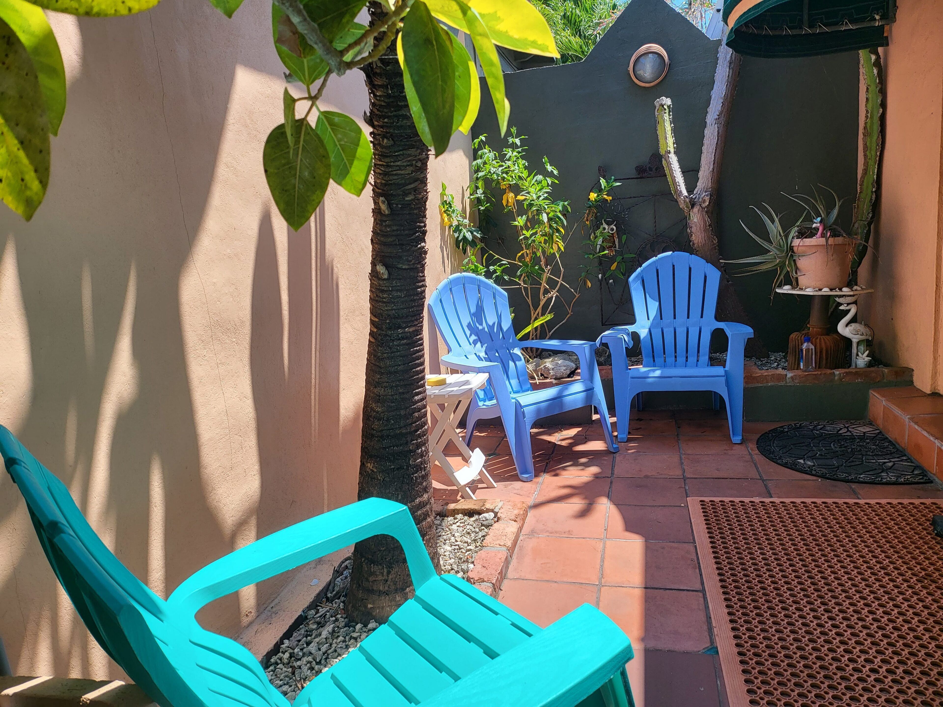 A patio area with two blue chairs, a small table, and a potted plant.