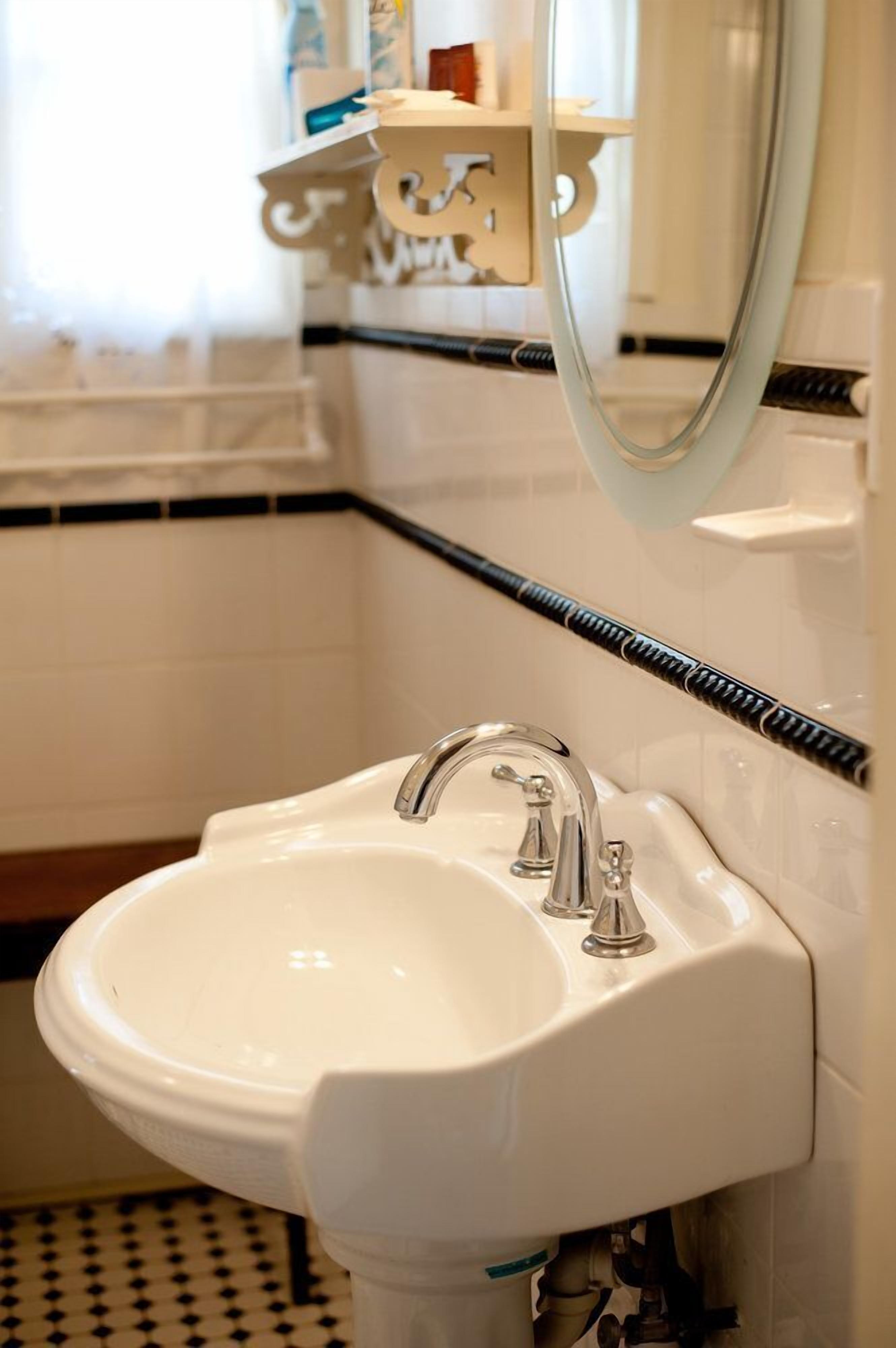 Un baño con un lavamanos blanco, un espejo y un suelo con baldosas blanco y negro.