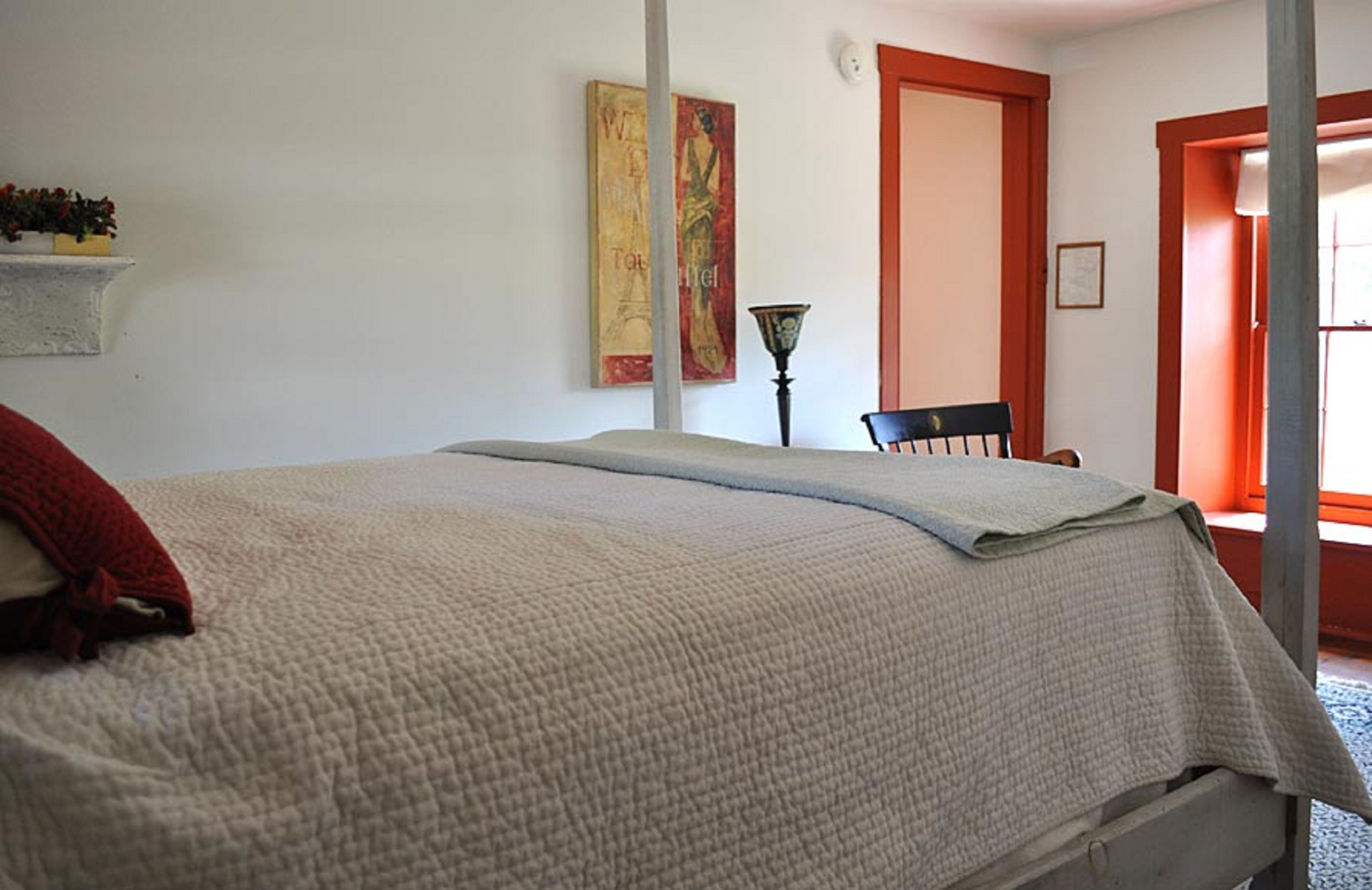 Une chambre à coucher avec un lit, une chaise, une lampe et un tableau au mur.