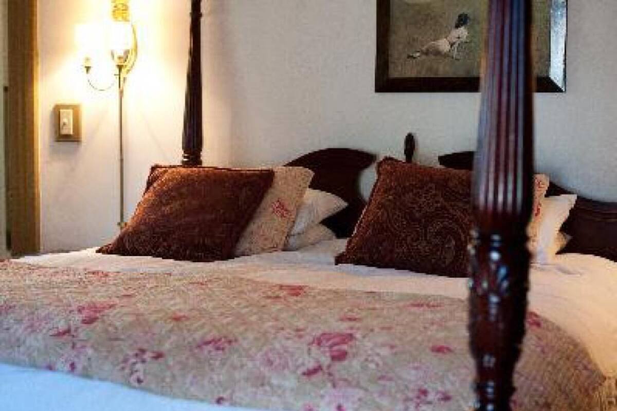 A neatly made bed with a floral bedspread and several pillows, a wall-mounted lamp, and a framed picture above the bed.