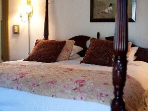 A neatly made bed with a floral bedspread and several pillows, a wall-mounted lamp, and a framed picture above the bed. - Ash Mill Farm Bed & Breakfast (Holicong)
