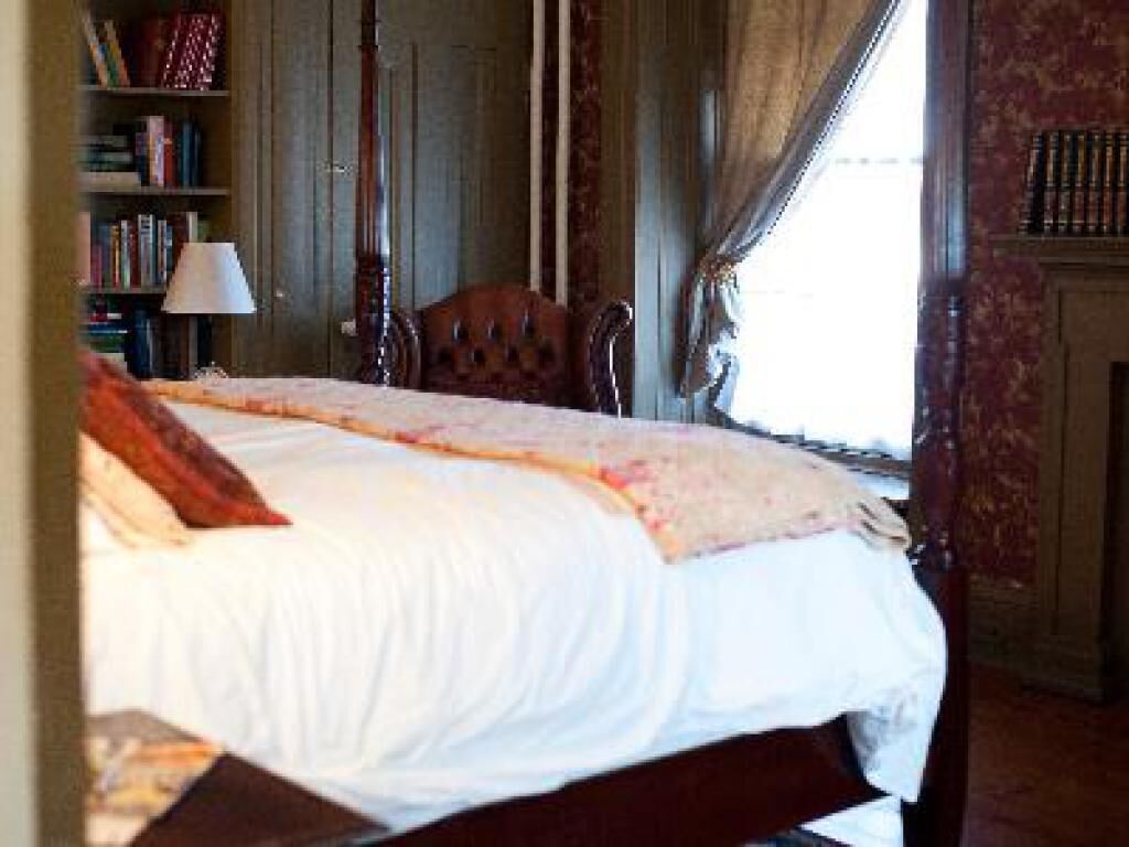 A bedroom with a large bed, a wooden chair, a bookshelf, and a window with curtains.