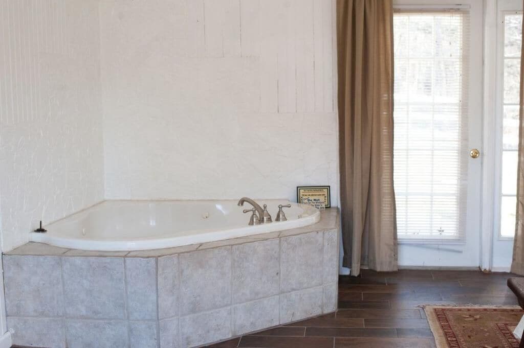 A bathroom with a freestanding bathtub, a tiled floor, and a door with curtains.