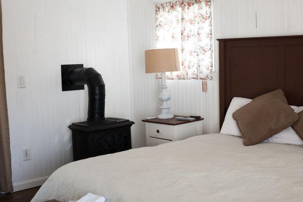 Une chambre à coucher avec un lit, une table de chevet avec une lampe, un radiateur fixé au mur et une fenêtre ornée de rideaux à motifs floraux.