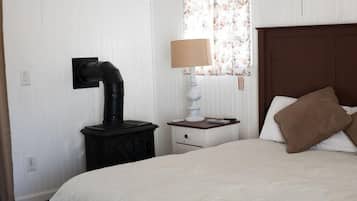 Une chambre à coucher avec un lit, une table de chevet avec une lampe, un radiateur fixé au mur et une fenêtre ornée de rideaux à motifs floraux.