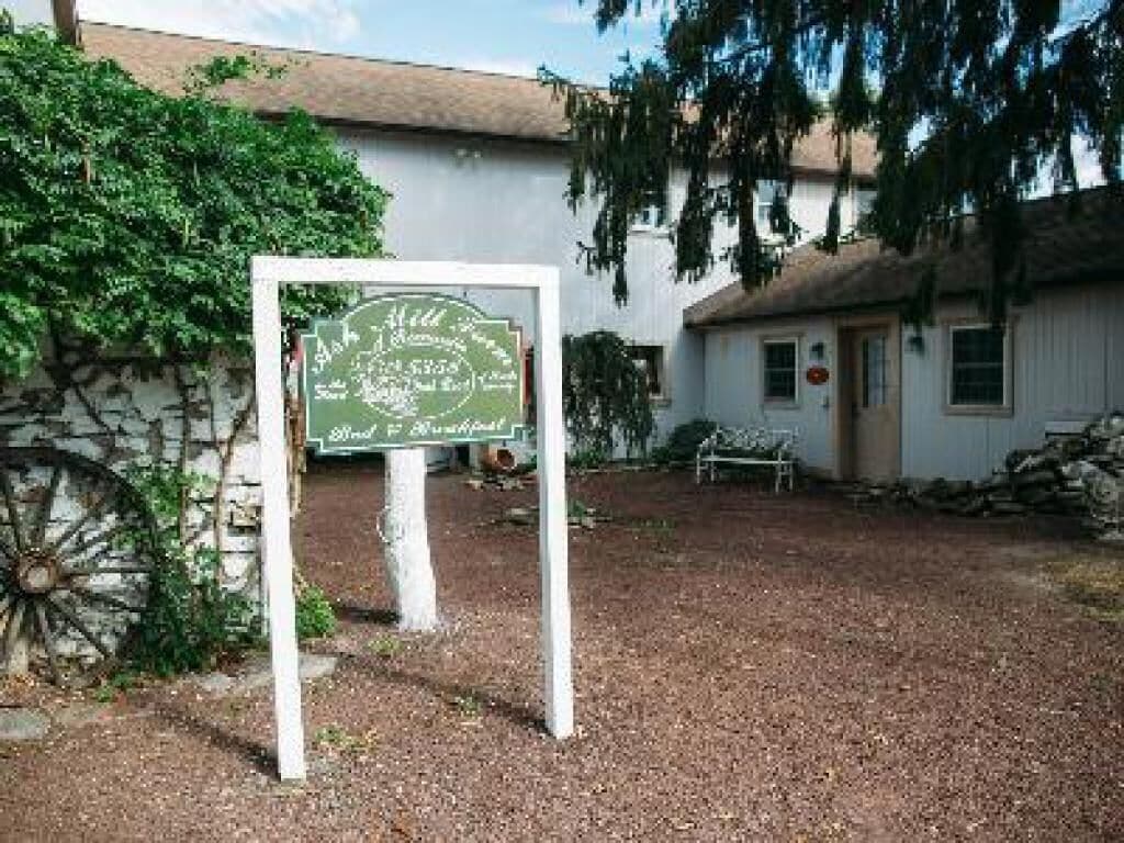 A sign with text, a building, and a wheel in a courtyard.