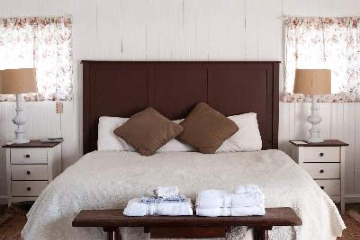 A neatly made bed with two pillows, a bedside table with a lamp, and a window with floral curtains.