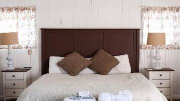 Una cama bien hecha con dos almohadas, una mesita de noche con una lámpara y una ventana con cortinas florales.