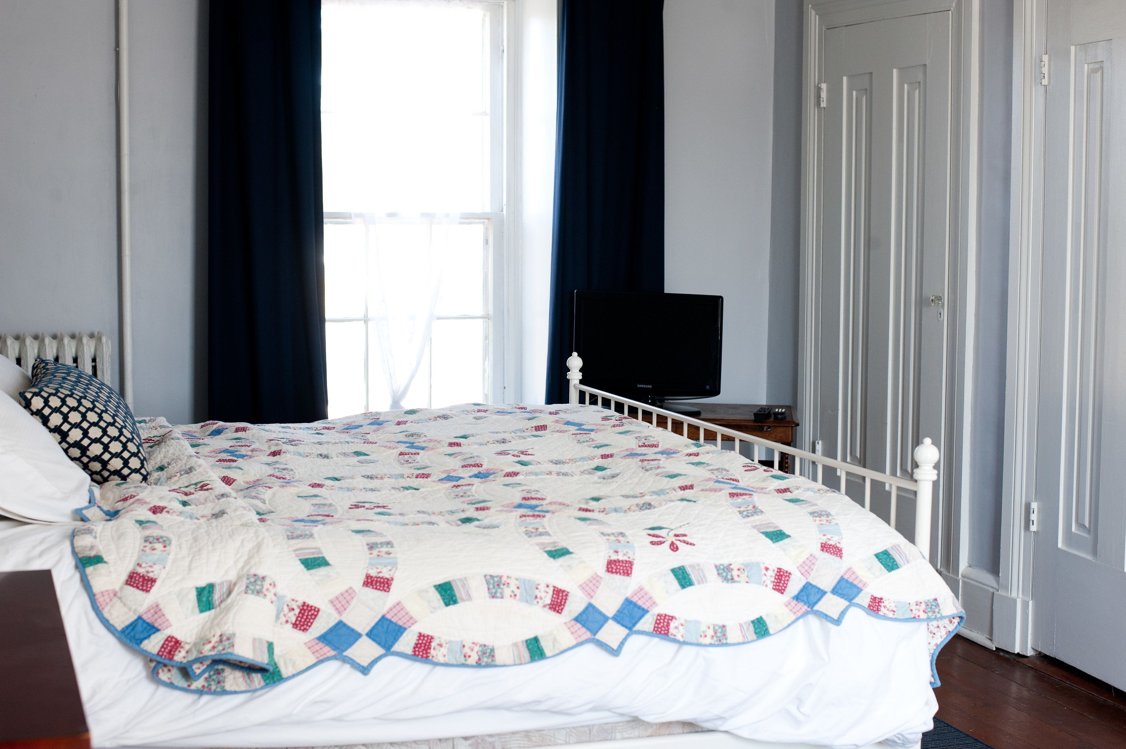 A bedroom with a bed, a television on a stand, a window with curtains, and a door.