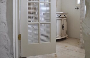 A white door with a window, a white cabinet with black handles, and a tiled floor.