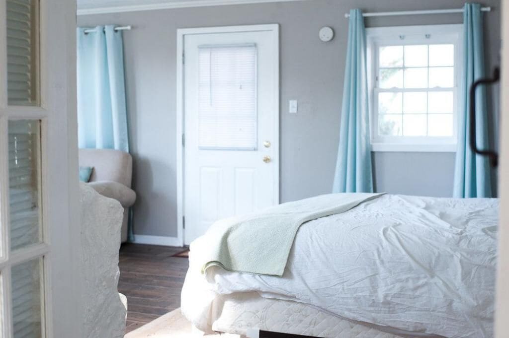A bedroom with a bed, a chair, a door, and curtains.