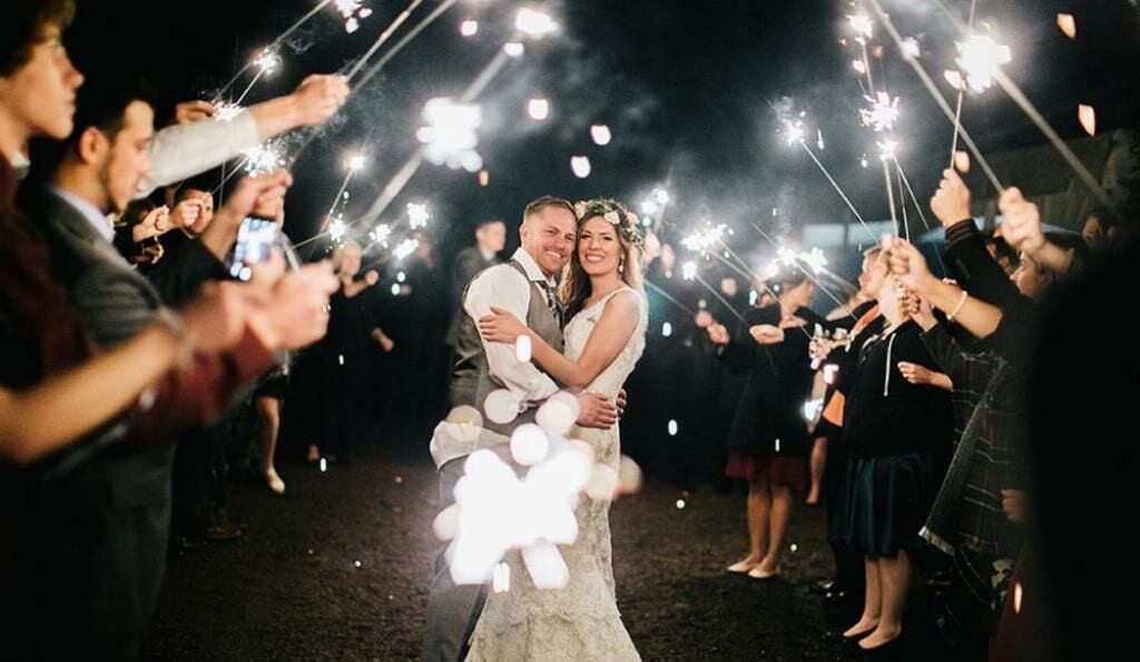 Un couple s’embrasse, entouré d’invités tenant des bâtonnets lumineux.