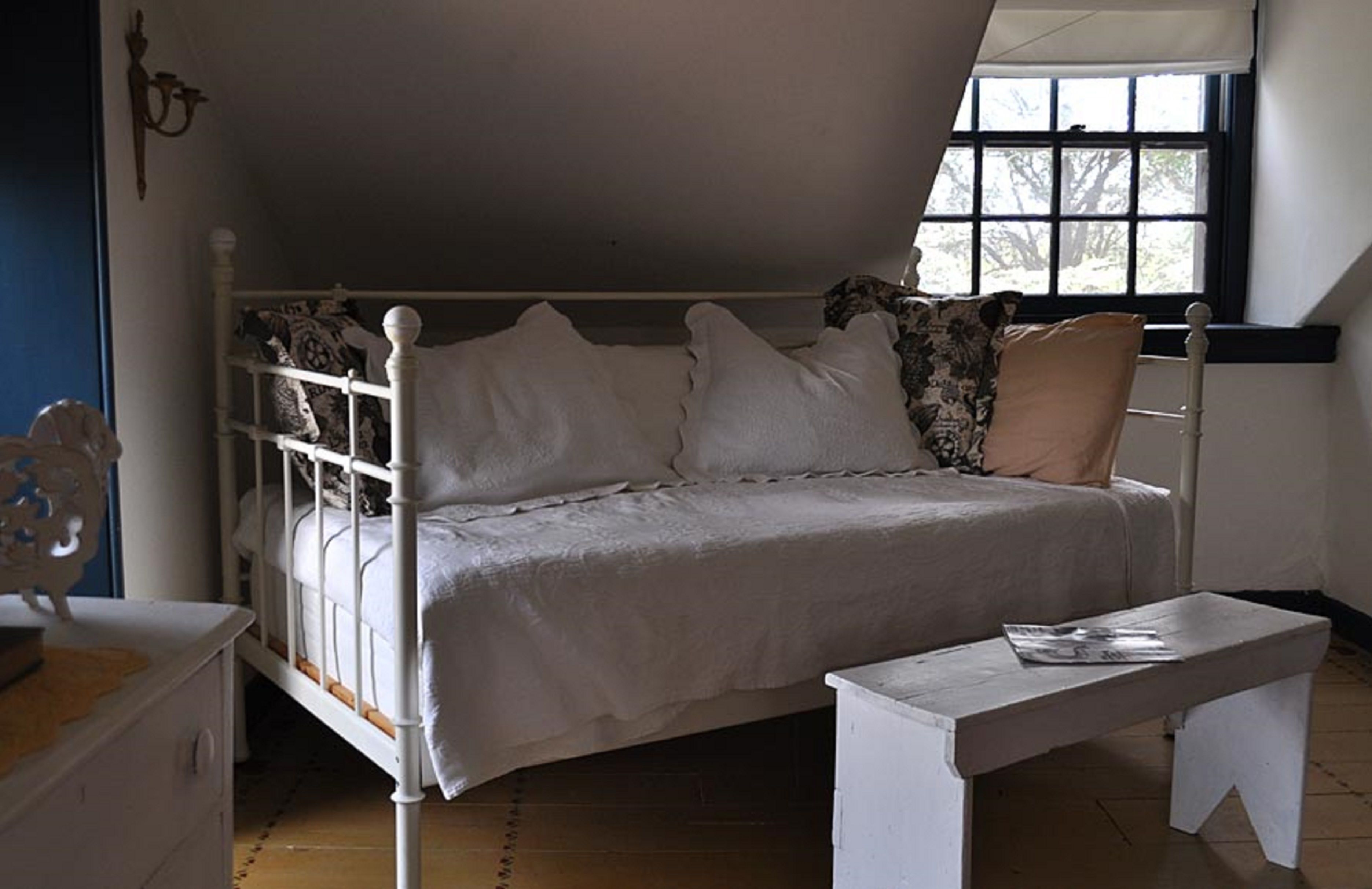 Un dormitorio con una cama blanca, un banco de madera y una ventana con vistas a árboles.