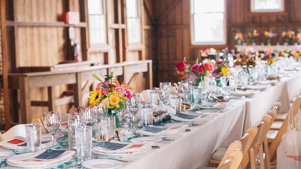 A long dining table set with glassware, plates, and colorful floral centerpieces in a rustic wooden room. - Ash Mill Farm Bed & Breakfast (Holicong)