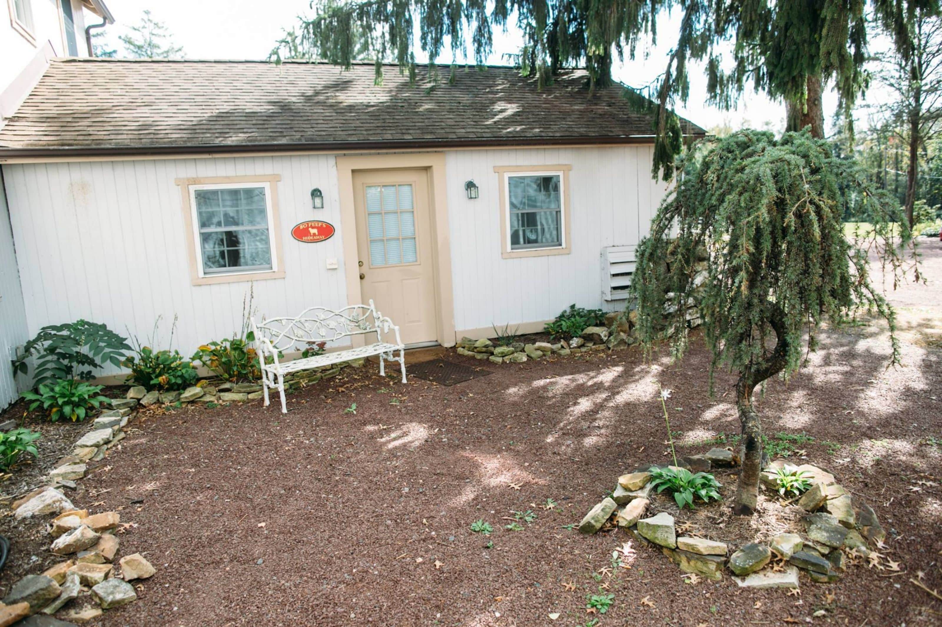 A small white building with a door, two windows, and a bench in front.
