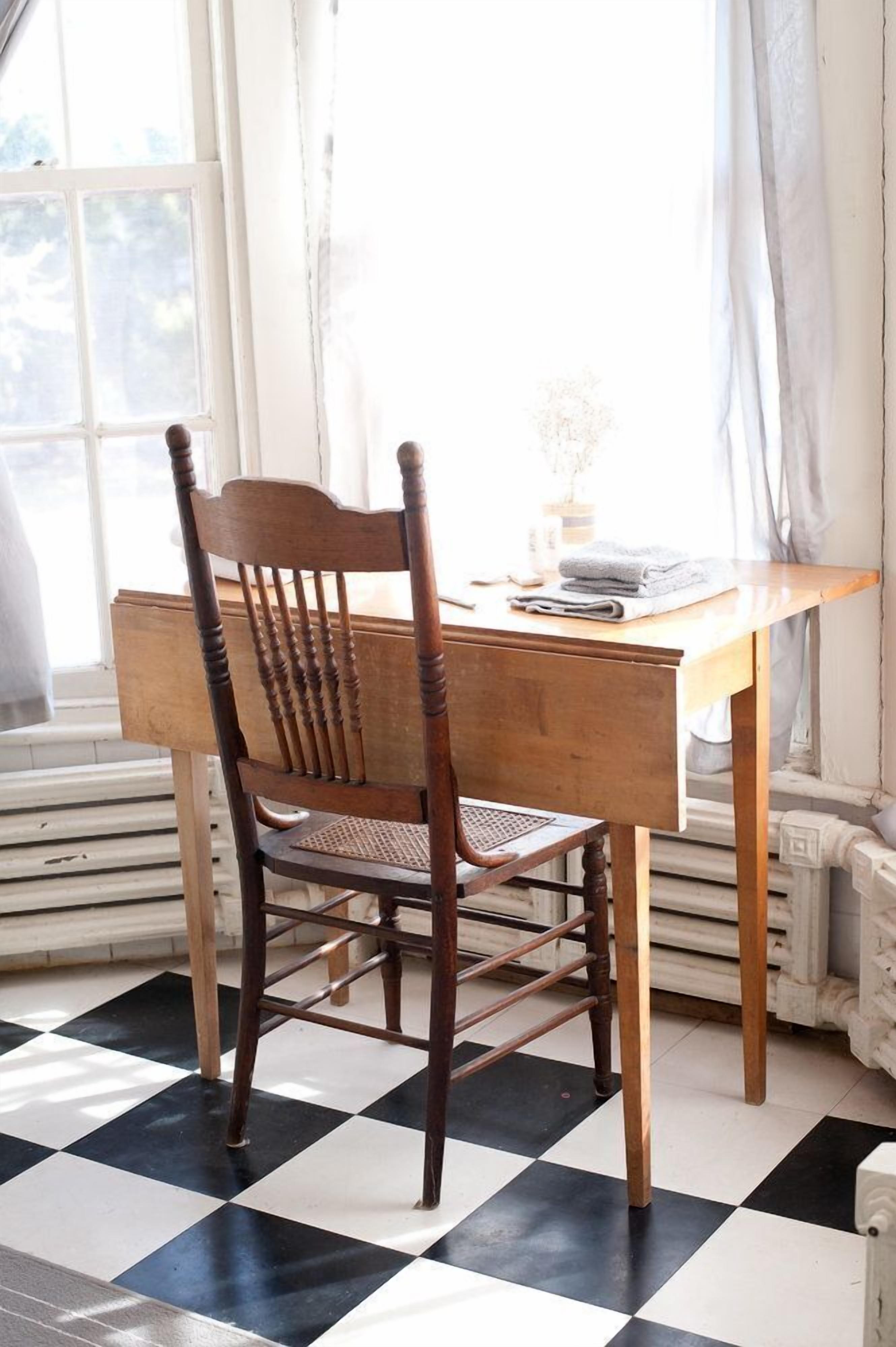 A wooden chair and table in a room with a checkered floor and a window with curtains.