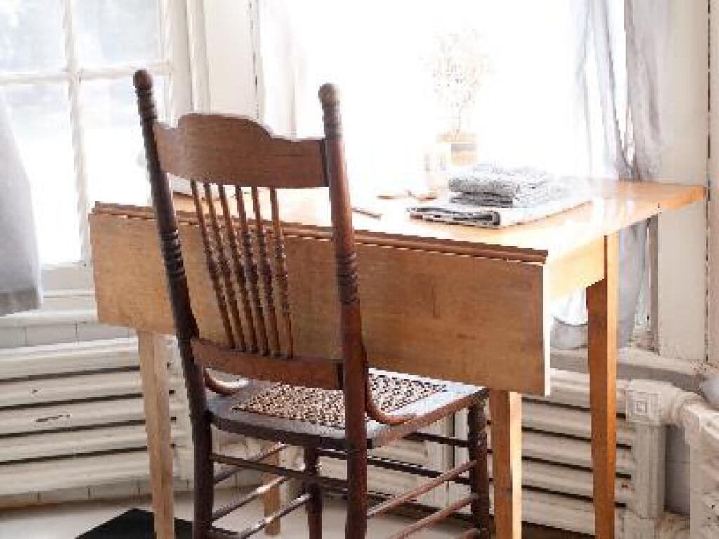 A wooden chair with a woven seat and backrest, positioned at a wooden table with a book and a vase.