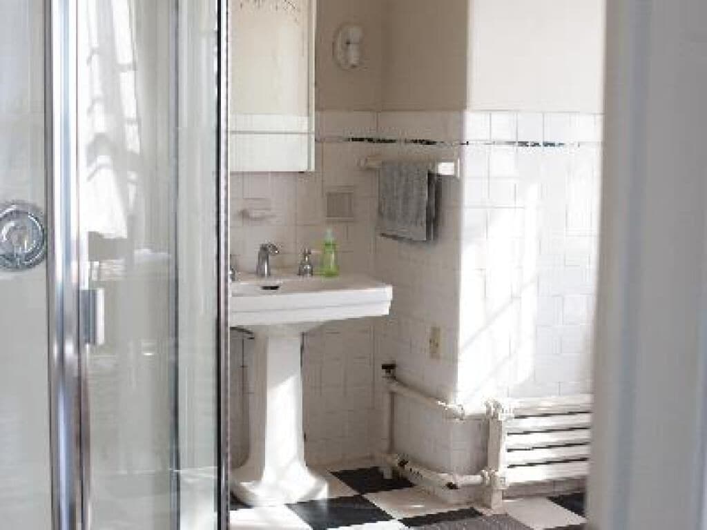 Casa de banho com cabine de duche em vidro, lavatório branco e chão em azulejo.