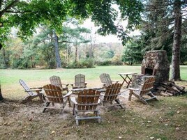 A rustic outdoor seating area with Adirondack chairs and a stone fire pit.
