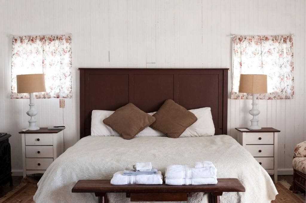 A neatly arranged bedroom with a large bed, two bedside tables, a bedside lamp, and a small table with folded towels.