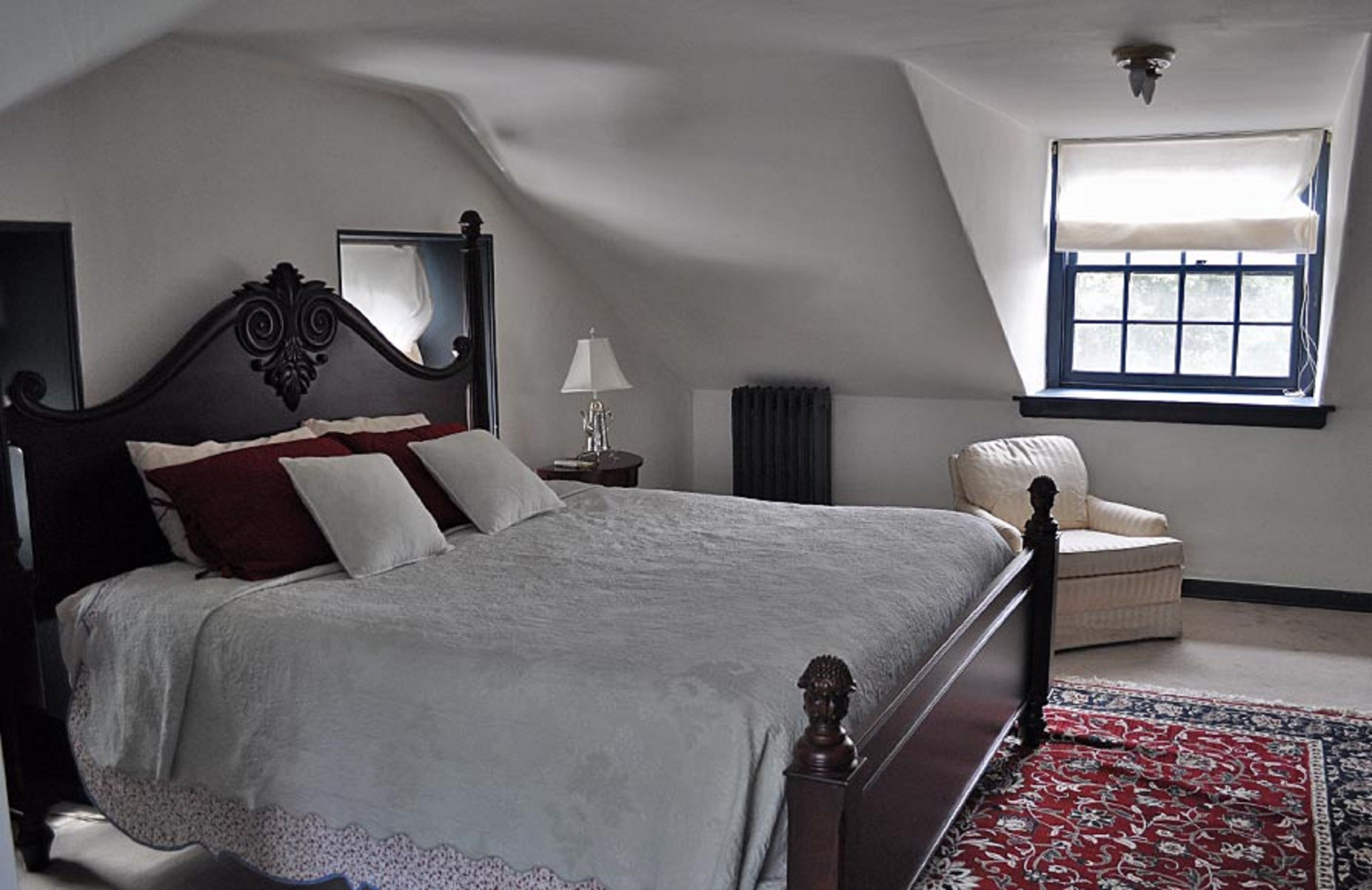 A bedroom with a large bed, a chair, a window, and a mirror.