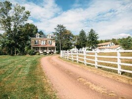 A rural road leading to a large house with a white fence.