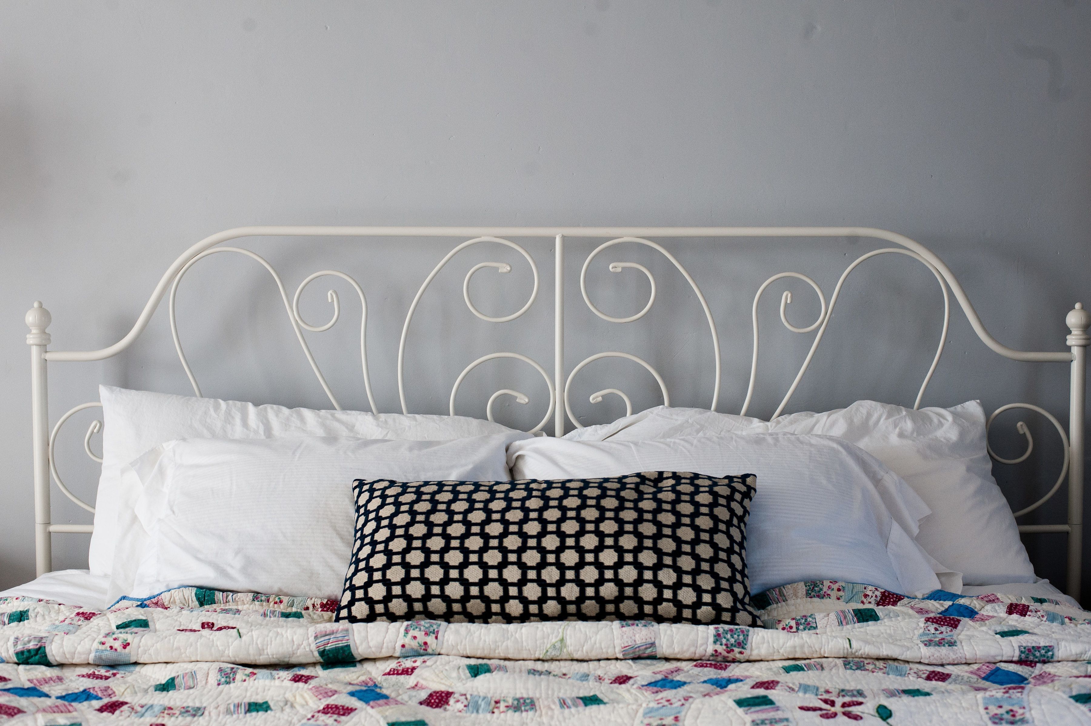 A bed with a white metal frame, white pillows, and a quilt with a patchwork design.
