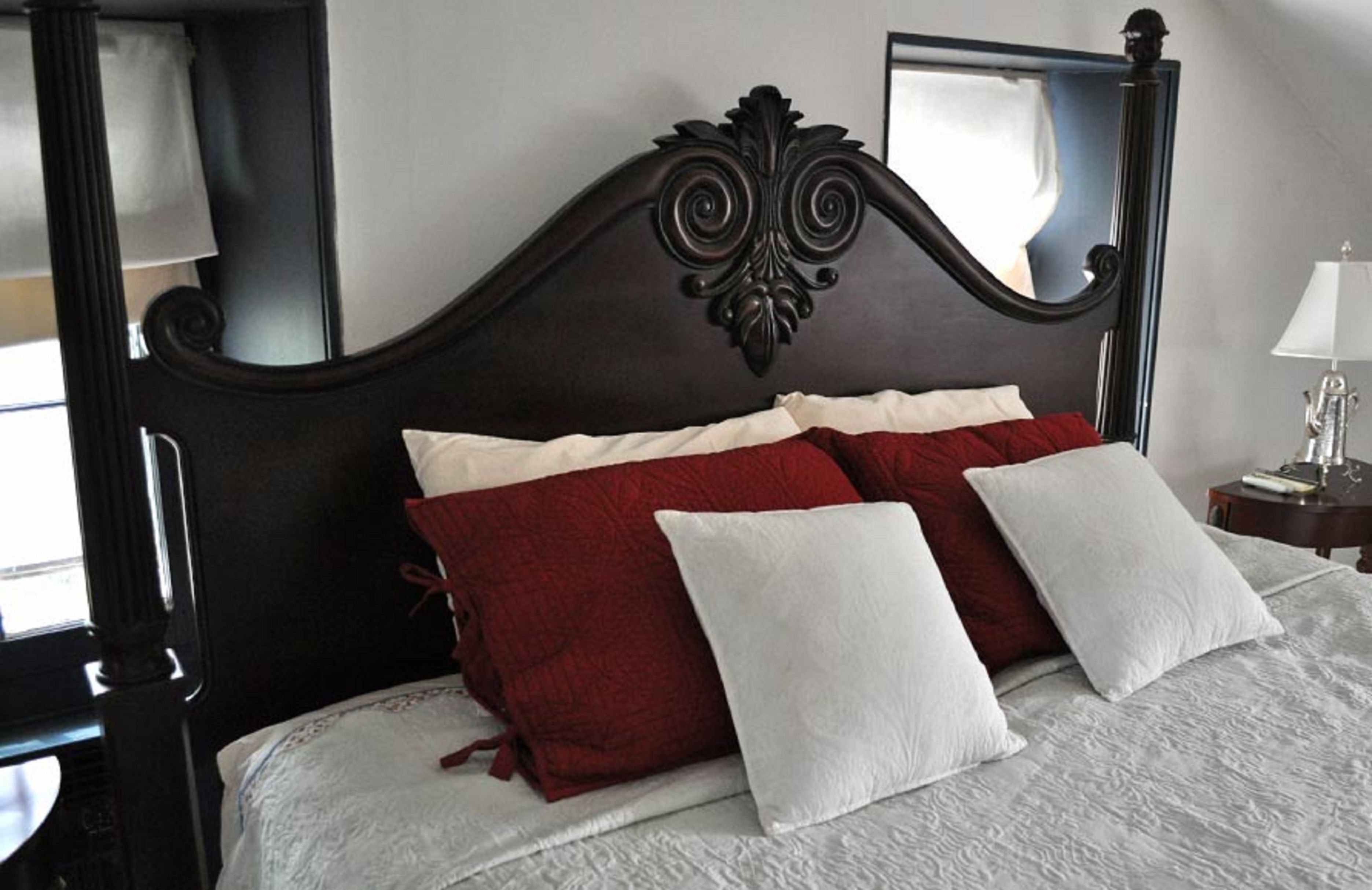 A bed with a dark headboard, white and red pillows, and a white bedspread.