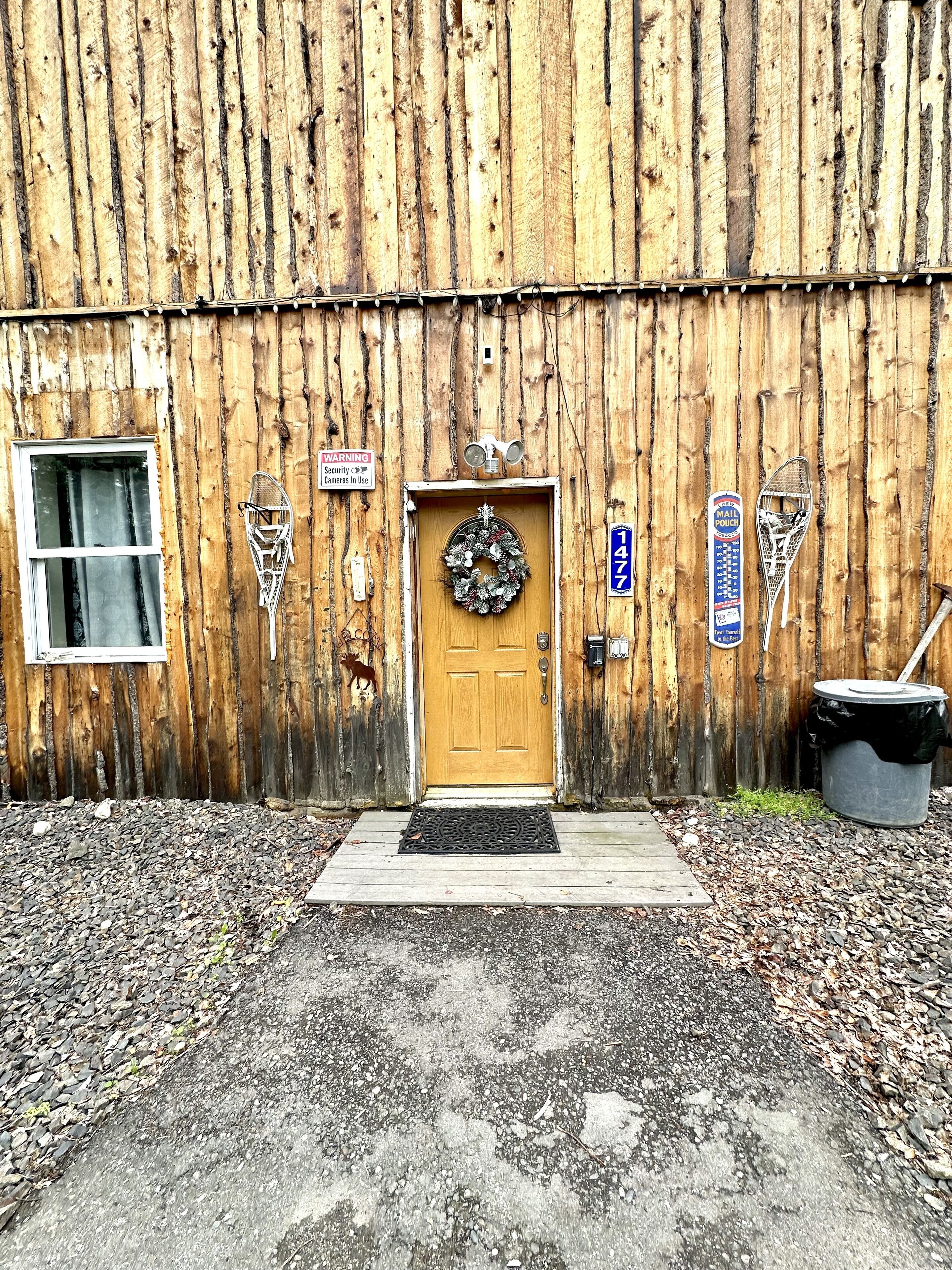 A rustic wooden building with a wooden door, a mailbox, and a security camera.