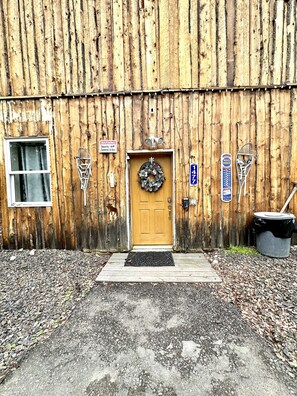 Un bâtiment rustique en bois, doté d’une porte en bois, d’une boîte aux lettres et d’une caméra de surveillance.