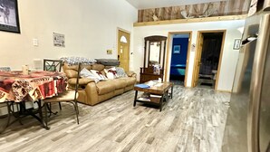 Amplia sala de estar con piso de madera, sofá de cuero marrón, una mesa de centro y un ventilador de techo.