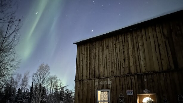 Un edificio de madera con una ventana y una puerta, rodeado de nieve y árboles.