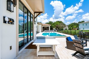 Et moderne poolområde udendørs med en hvid terrasse, liggestole og et spisebord.