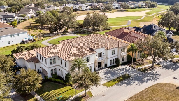 A residential area with a large white house featuring a red-tiled roof, surrounded by trees and a golf course in the background. - NEW FURNITURE Aug 2026 | Movie Theater & Games Room | Golf Course Views (Kissimmee)