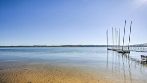 Una spiaggia tranquilla con un molo di legno che si protende sull'acqua, un cielo sereno e una costa lontana.
