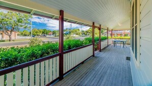 A covered porch with a view of a street and greenery.