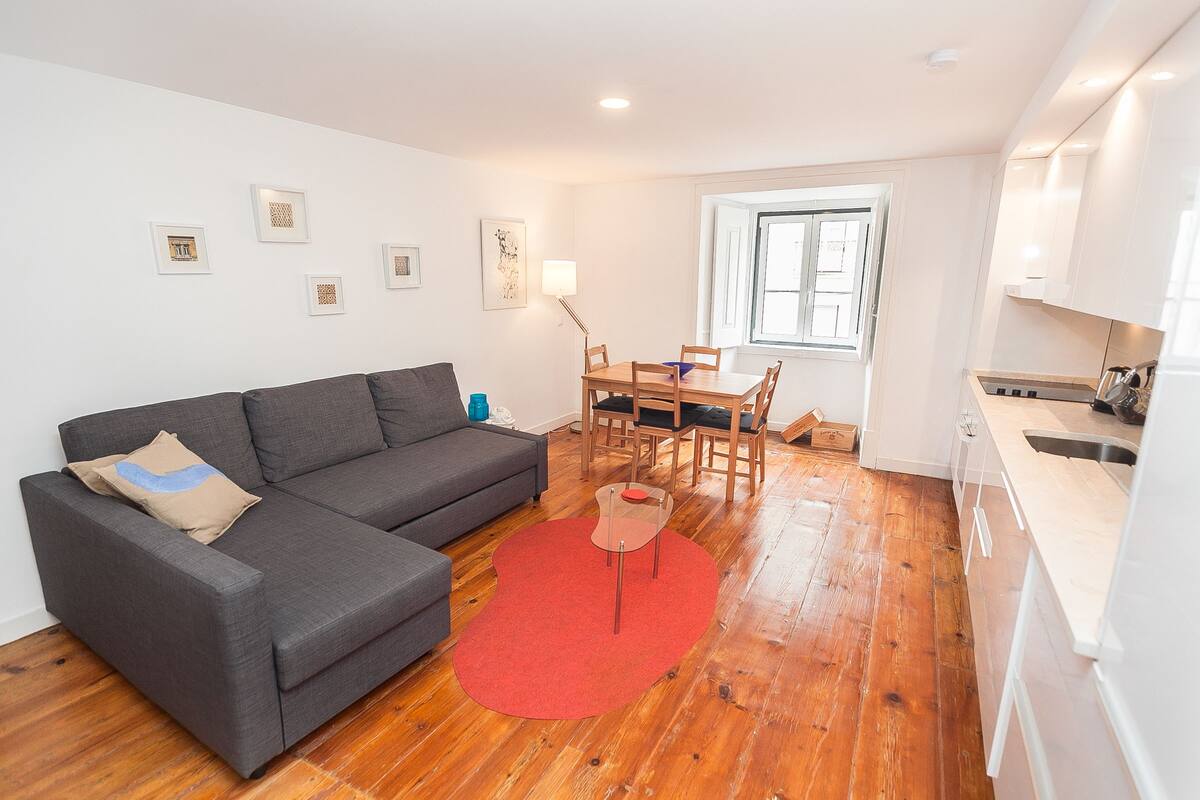 Una sala de estar moderna con un sofá gris, un tapete rojo y un comedor con sillas de madera y una mesa.