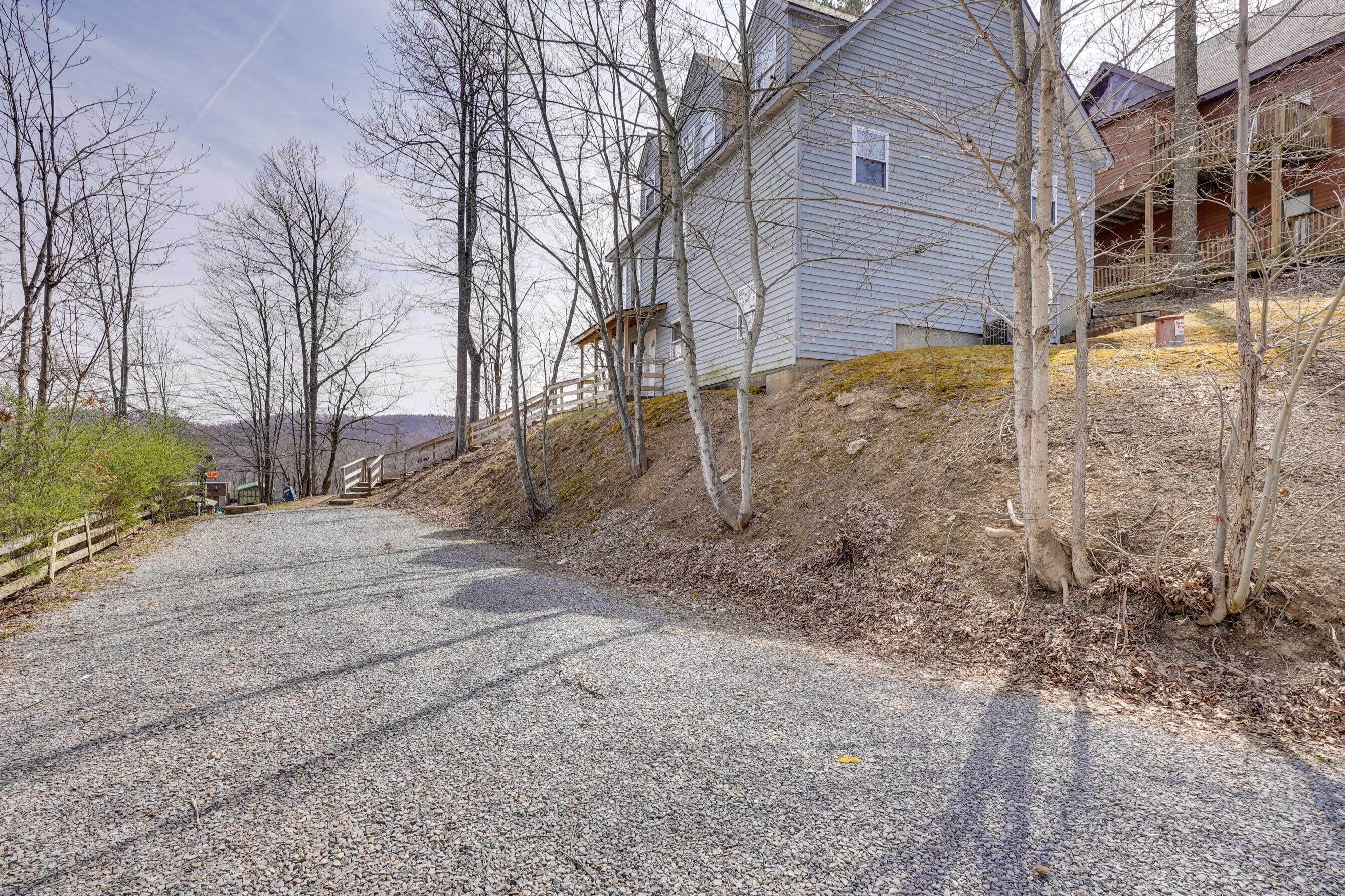 A gravel driveway leading to a house with a wooden fence and bare trees.