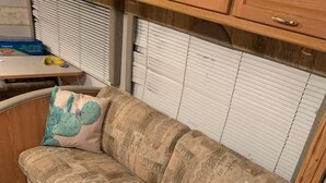 A sofa with patterned cushions, a small table with a banana, and a window with blinds. - NW Tucson - Roomy 20 Foot RV Nestled On A 3 Acre Property Sleeps 4 (Tucson)
