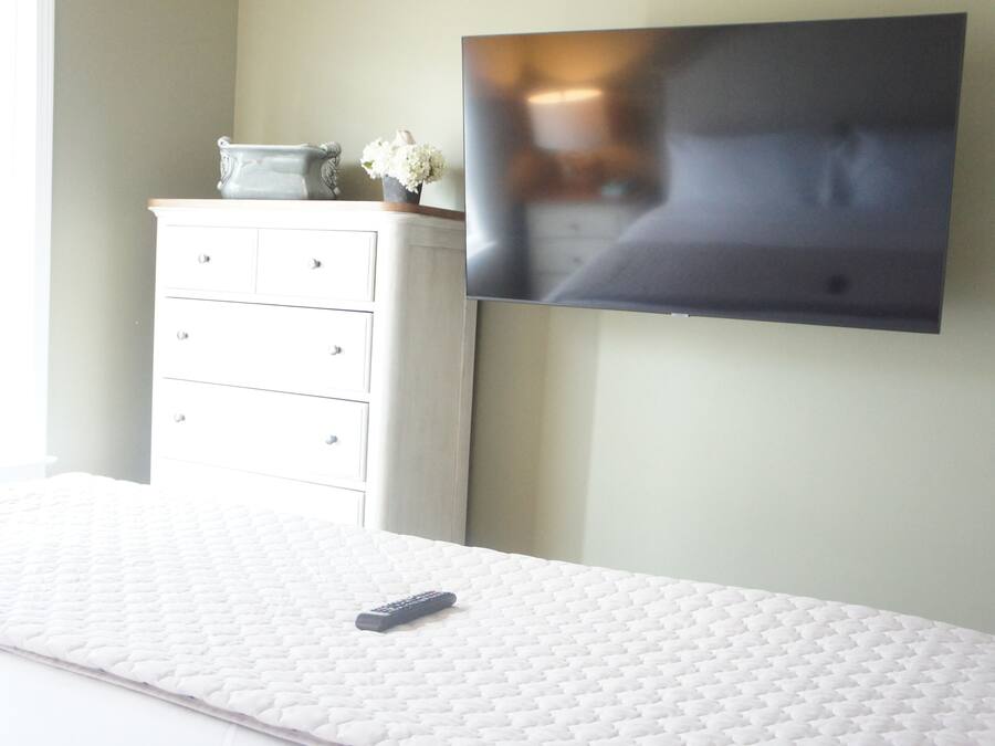 Un dormitorio con cama, televisor en la pared, cómoda y un jarrón con flores.