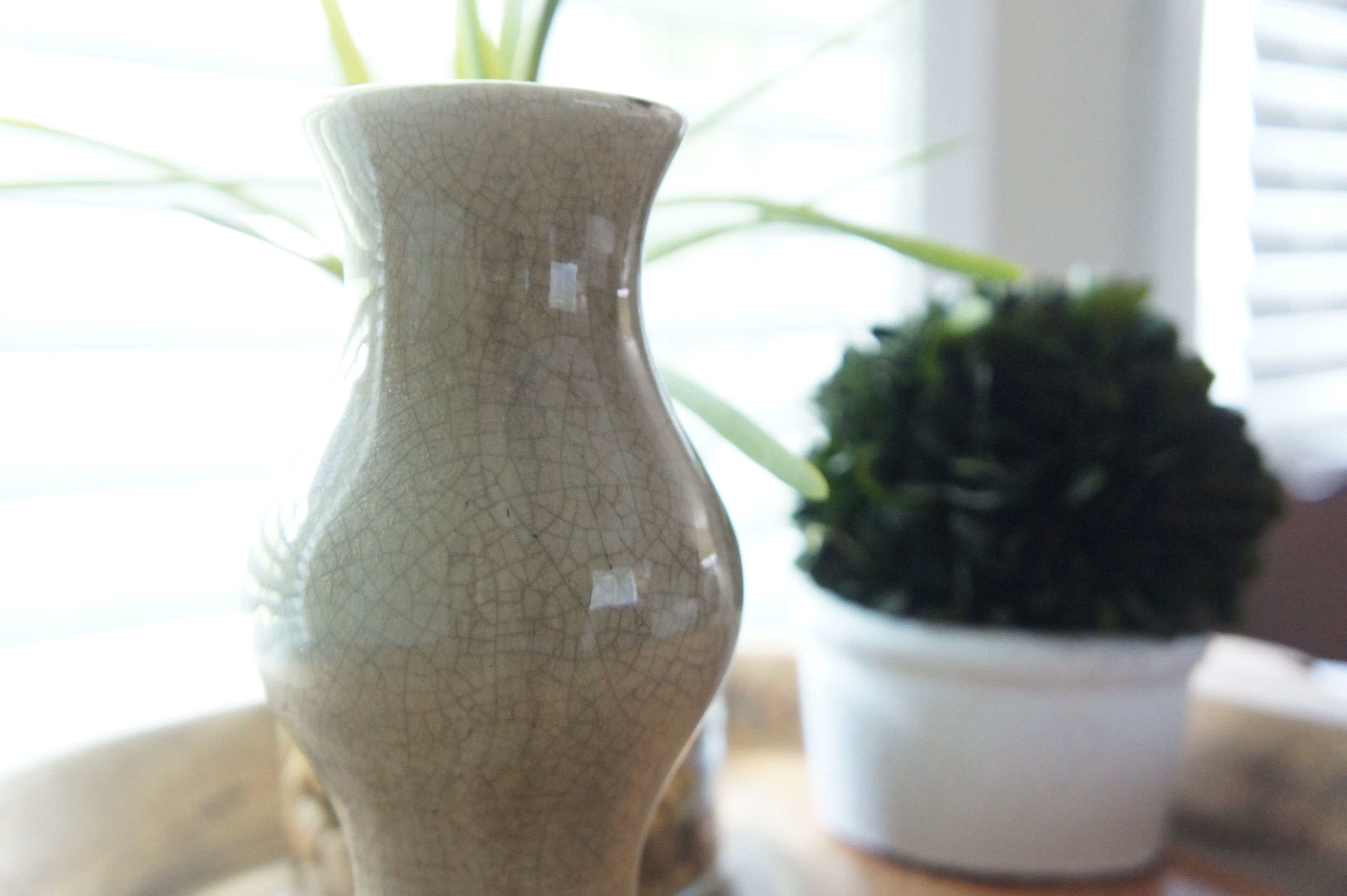 A ceramic vase with a textured surface, placed on a table next to a potted plant.