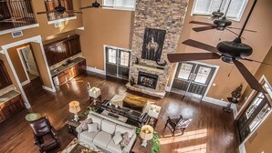 A spacious living area with a fireplace, seating, and a high ceiling with fans. - Magnolia Creek Lodge (Cottonwood)