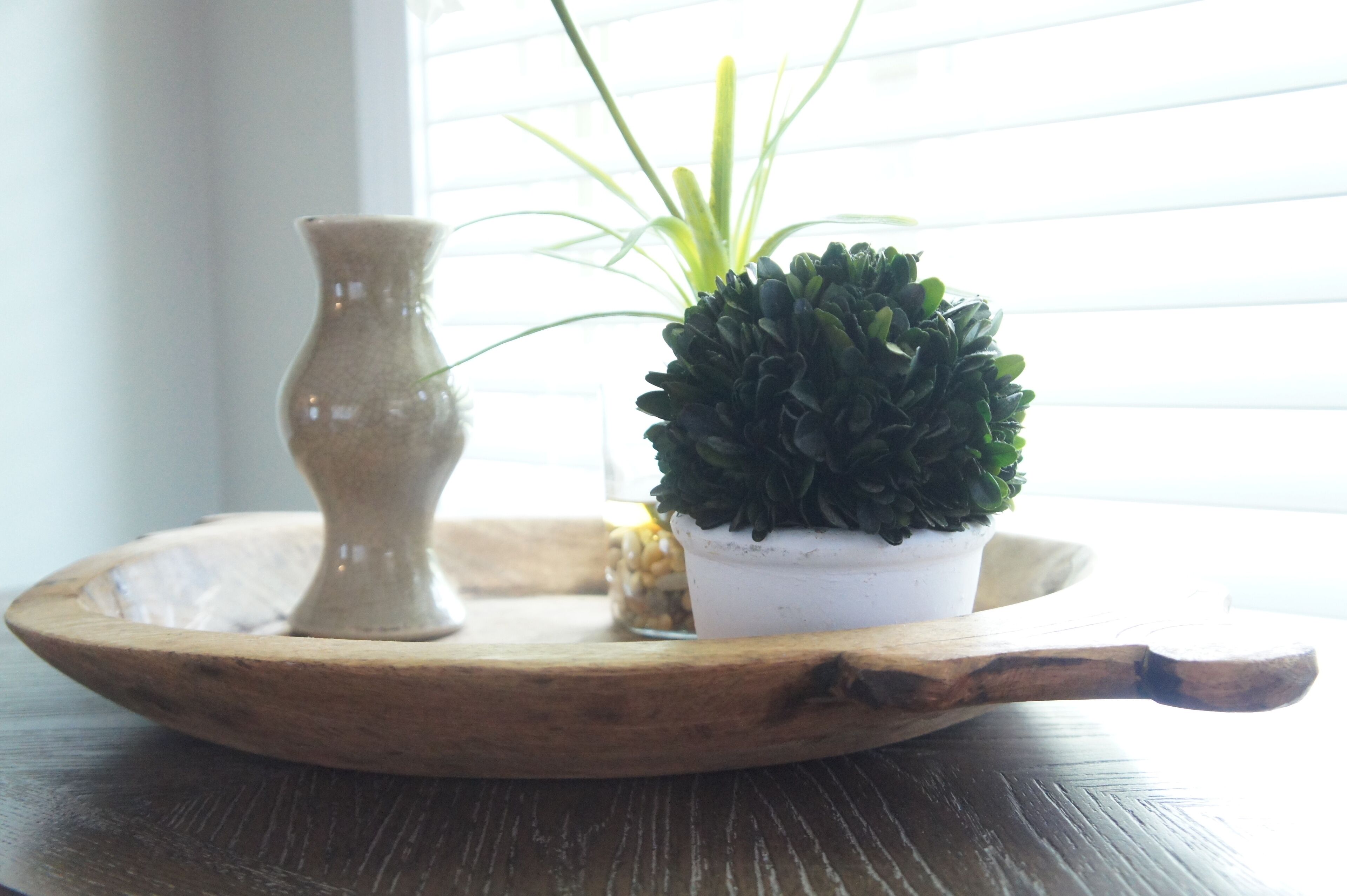 Una bandeja de madera con una pequeña planta en maceta y un jarrón sobre una mesa.