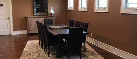 Un comedor con una mesa y sillas de madera, un tapete estampado y una pared marrón con ventanas.