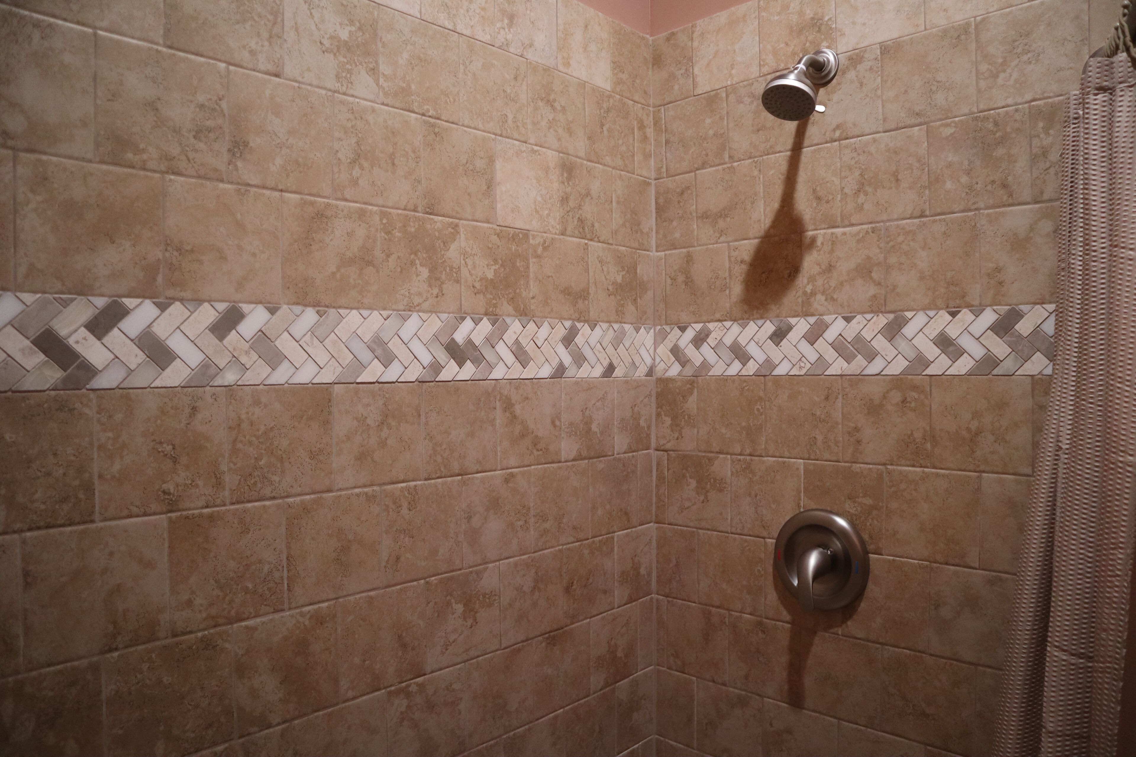 Un espace douche avec des carreaux de couleur beige et une bordure à motifs en chevrons.